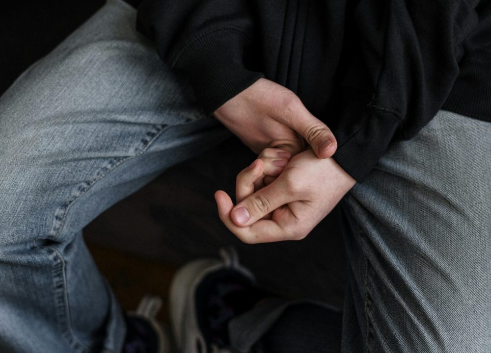 A young man in casual attire sitting with hands clasped, expressing contemplation.