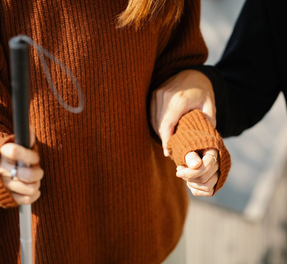 Close-up of two people holding hands, one with a walking cane symbolizing support and visual aid.